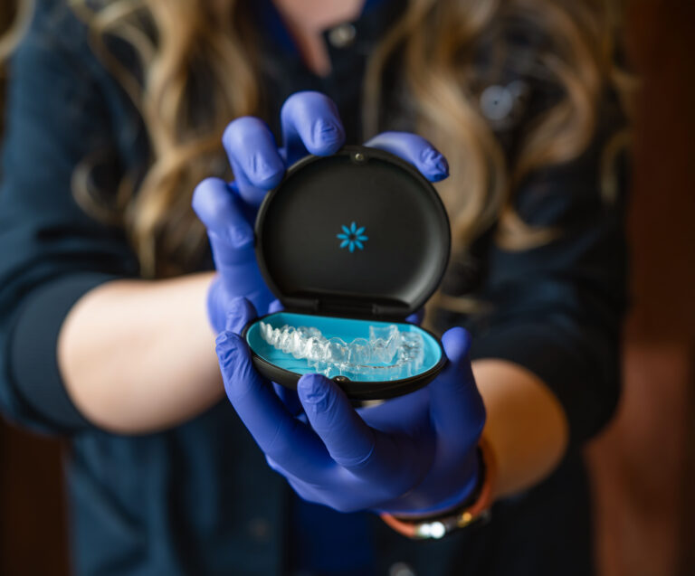 A cook nurse holding an invisalign box open with purple gloves.